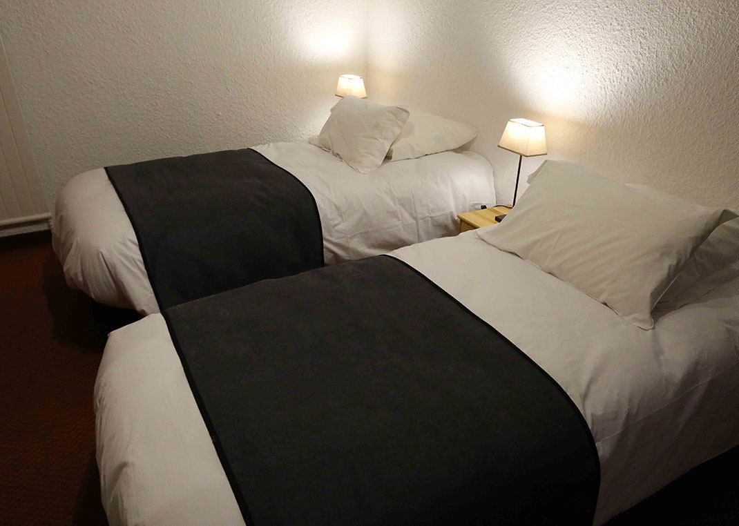 Two single beds with white and black bedding, each with a bedside table and lamp.