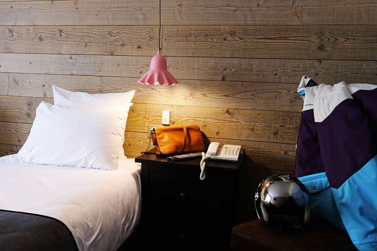 A wooden-paneled room with a bed, a nightstand with a lamp, a phone, and a helmet.