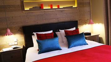 A hotel room with a wooden wall, a bed with red and blue bedding, two bedside tables with lamps, and a shelf with candles.