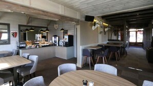 Un restaurante con zona de bar, varias opciones de asientos como mesas redondas y taburetes, y una barra visible con menú.