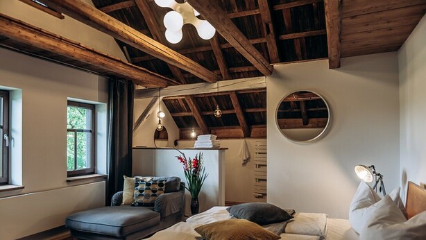 A bedroom with a loft bed, a small sofa, a bedside table with a lamp, and a window with curtains. - Berghütte Vogtland (Klingenthal)
