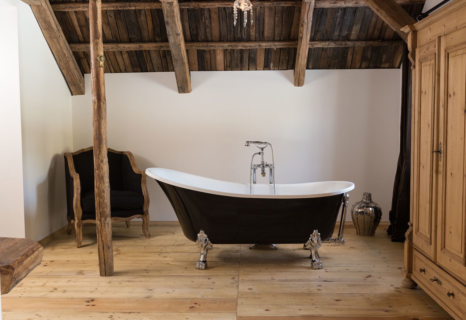 A rustic bathroom with a freestanding bathtub, wooden beams, and a wooden cabinet.