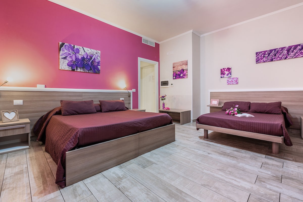 A bedroom with two beds, a wooden headboard, a bedside table with a lamp, and a wall-mounted artwork.