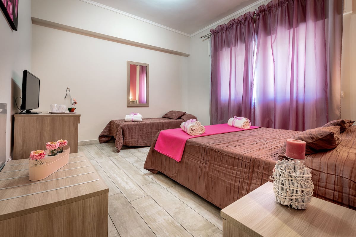 A hotel room with two beds, a TV, a mirror, and a small table with a vase.