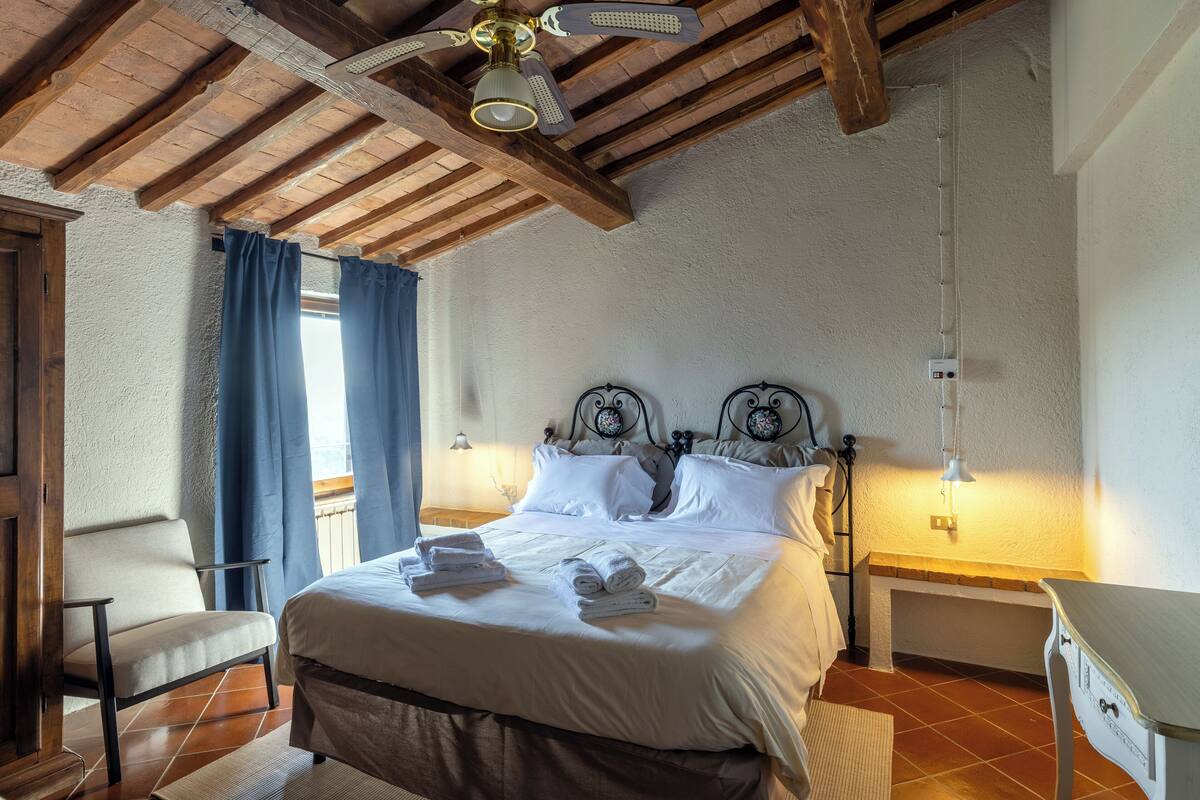 Une chambre avec un plafond en bois, un lit recouvert de draps blancs, une chaise et une table de chevet.
