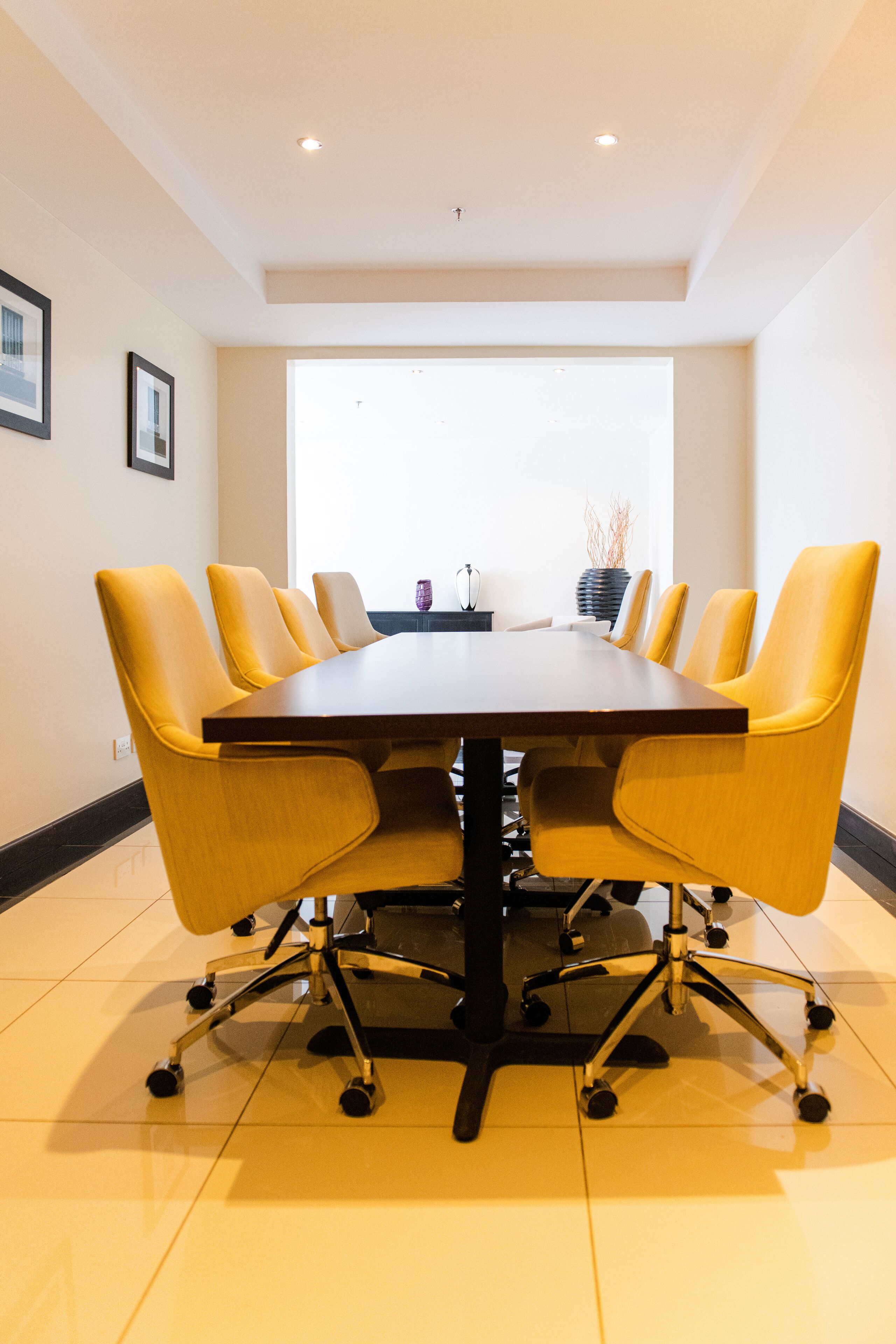 A conference room with a dark wooden table and yellow chairs.