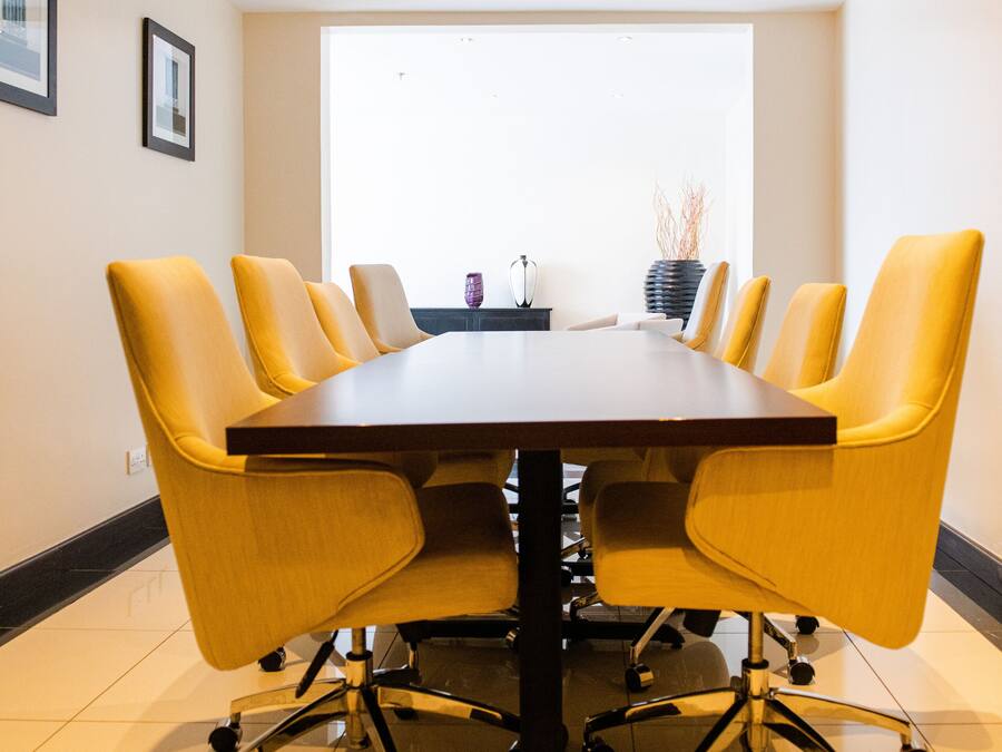 A conference room with a dark wooden table and yellow chairs.