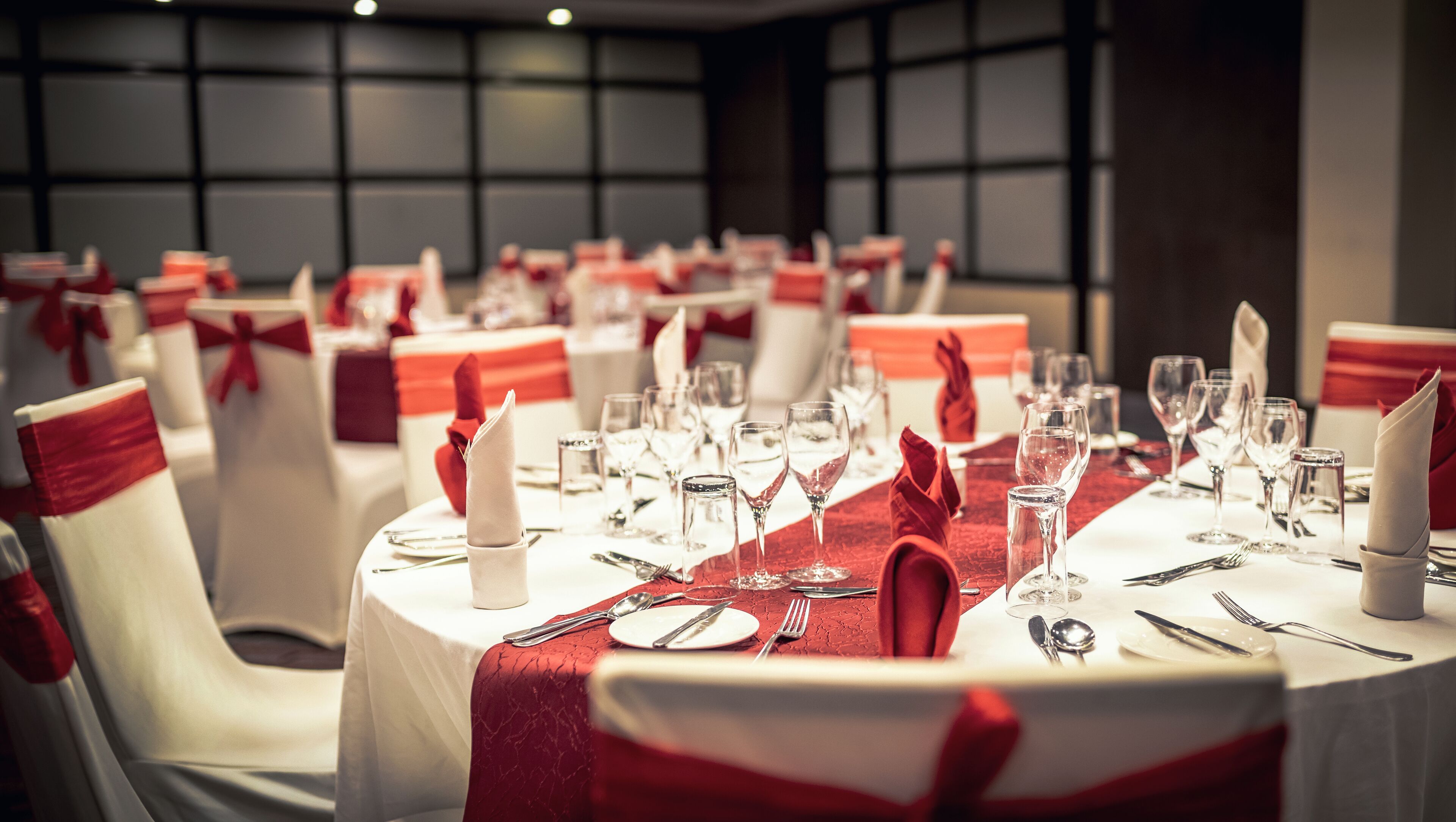 A banquet hall with round tables set for dining, each with white chairs and red sashes.