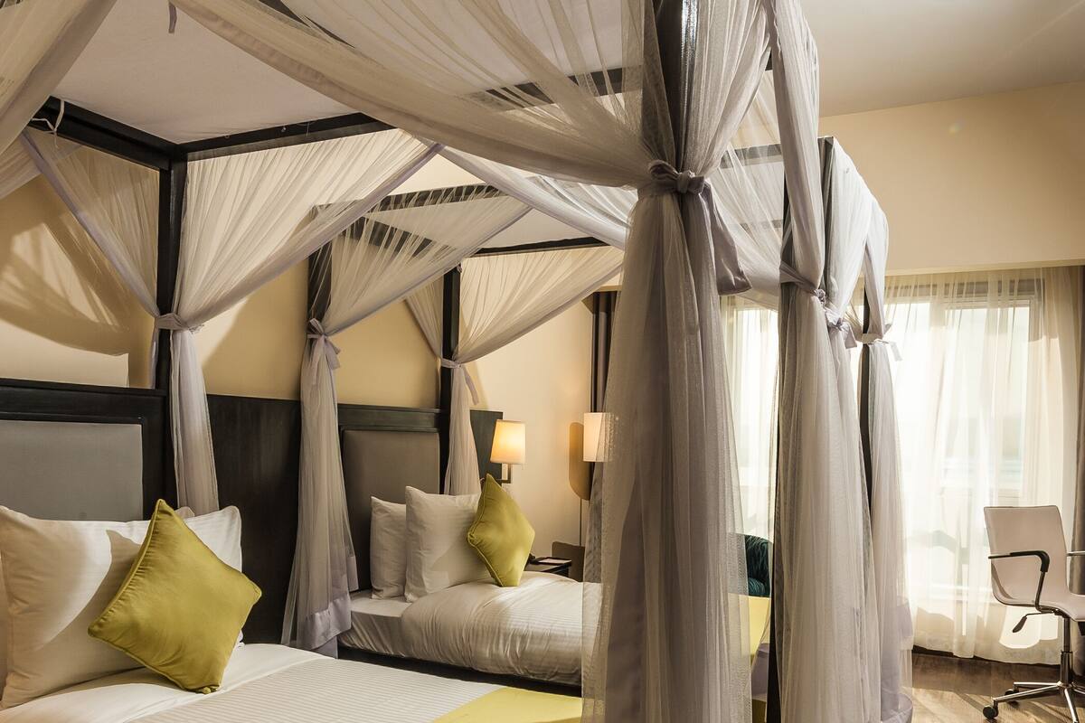 Ein Hotelzimmer mit einem Himmelsbett, einer grünen Tagesdecke, einem Nachttisch mit Lampe und einem Sessel.