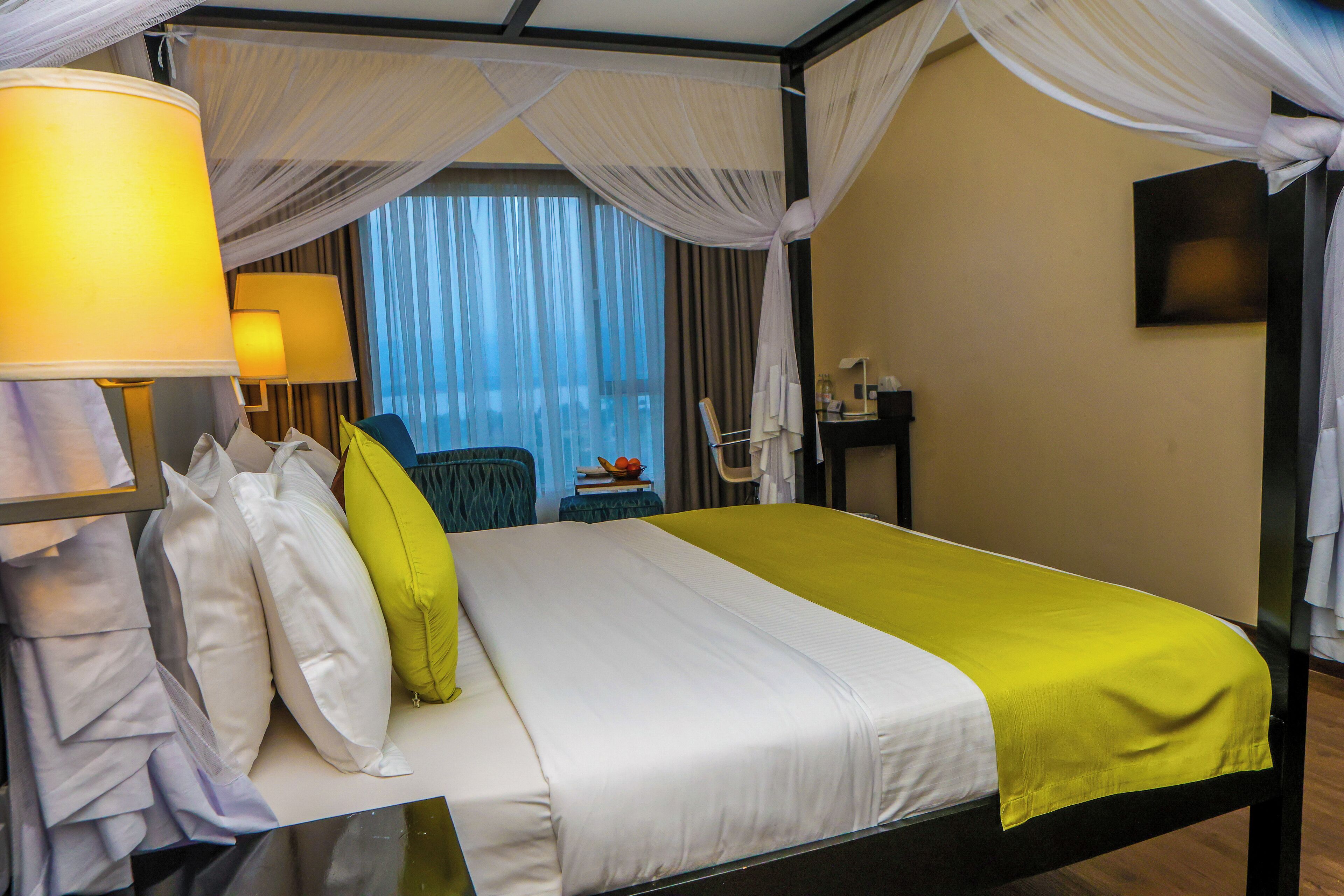 Een hotelkamer met een bed, nachtkastje, lamp en een raam met gordijnen.