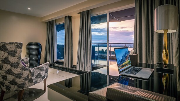 Habitación de hotel moderna con una mesa de vidrio, una computadora portátil, una lámpara y vistas a un puente y al paisaje urbano.