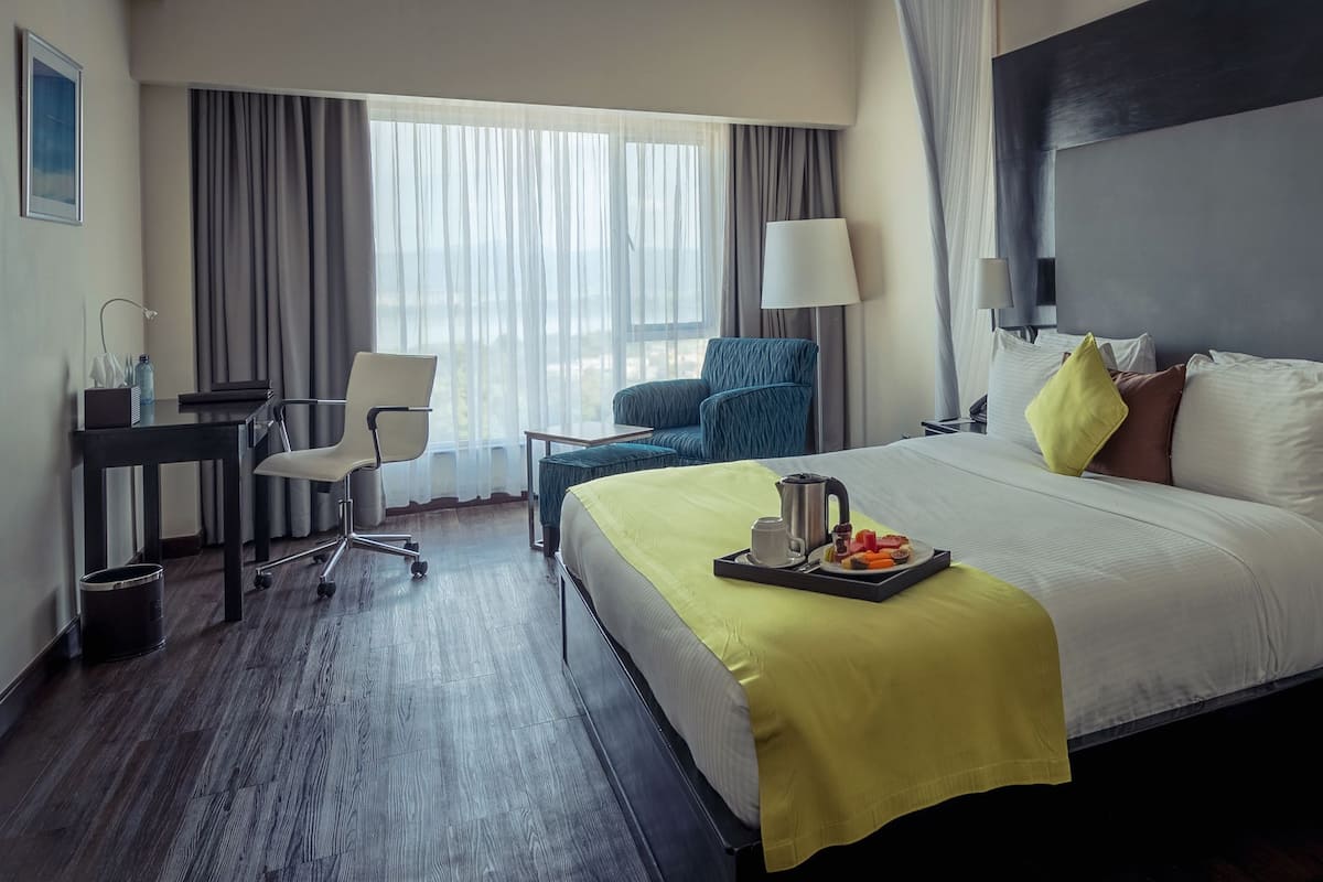 Ein Hotelzimmer mit einem großen Bett, einem Schreibtisch, einem Sessel und Blick auf die Stadt.