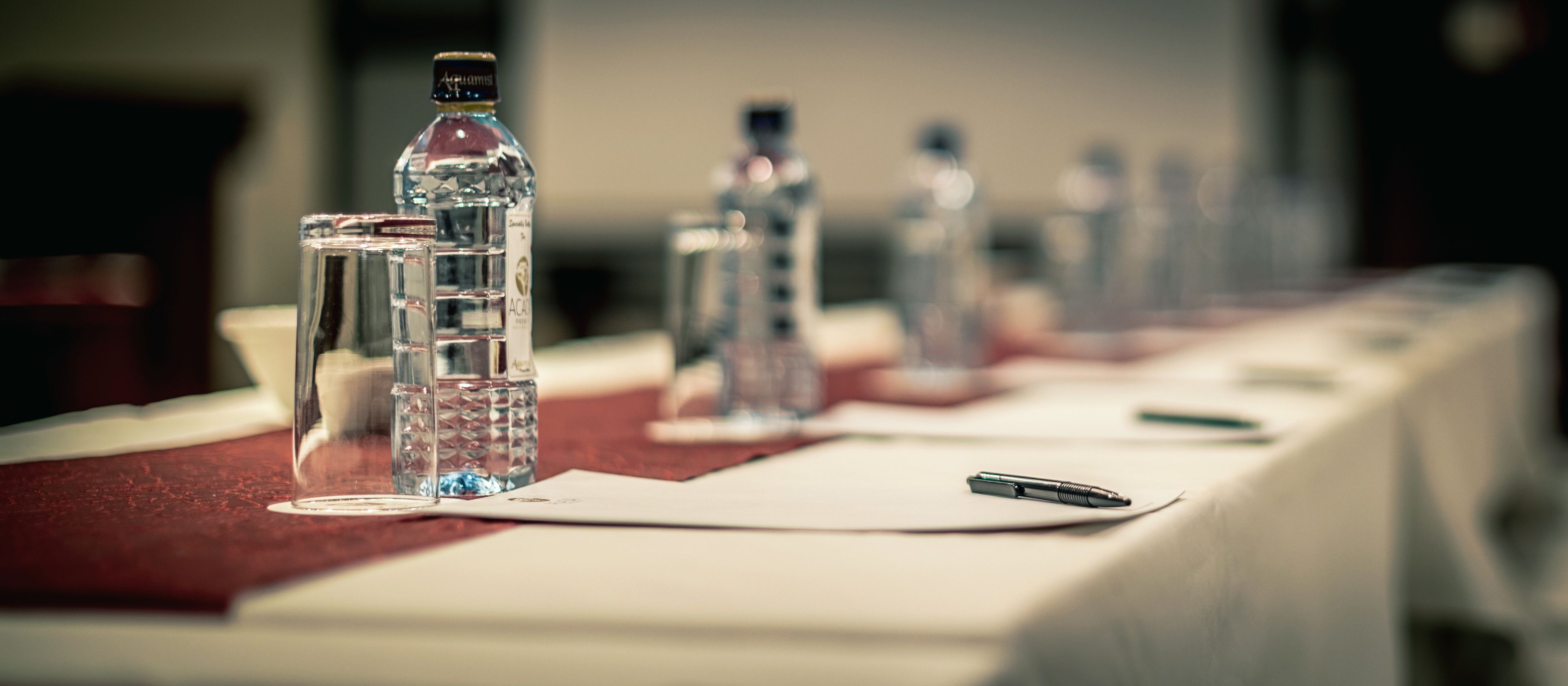 Una mesa con botellas de agua y un bolígrafo, evocando un ambiente de reunión o conferencia.