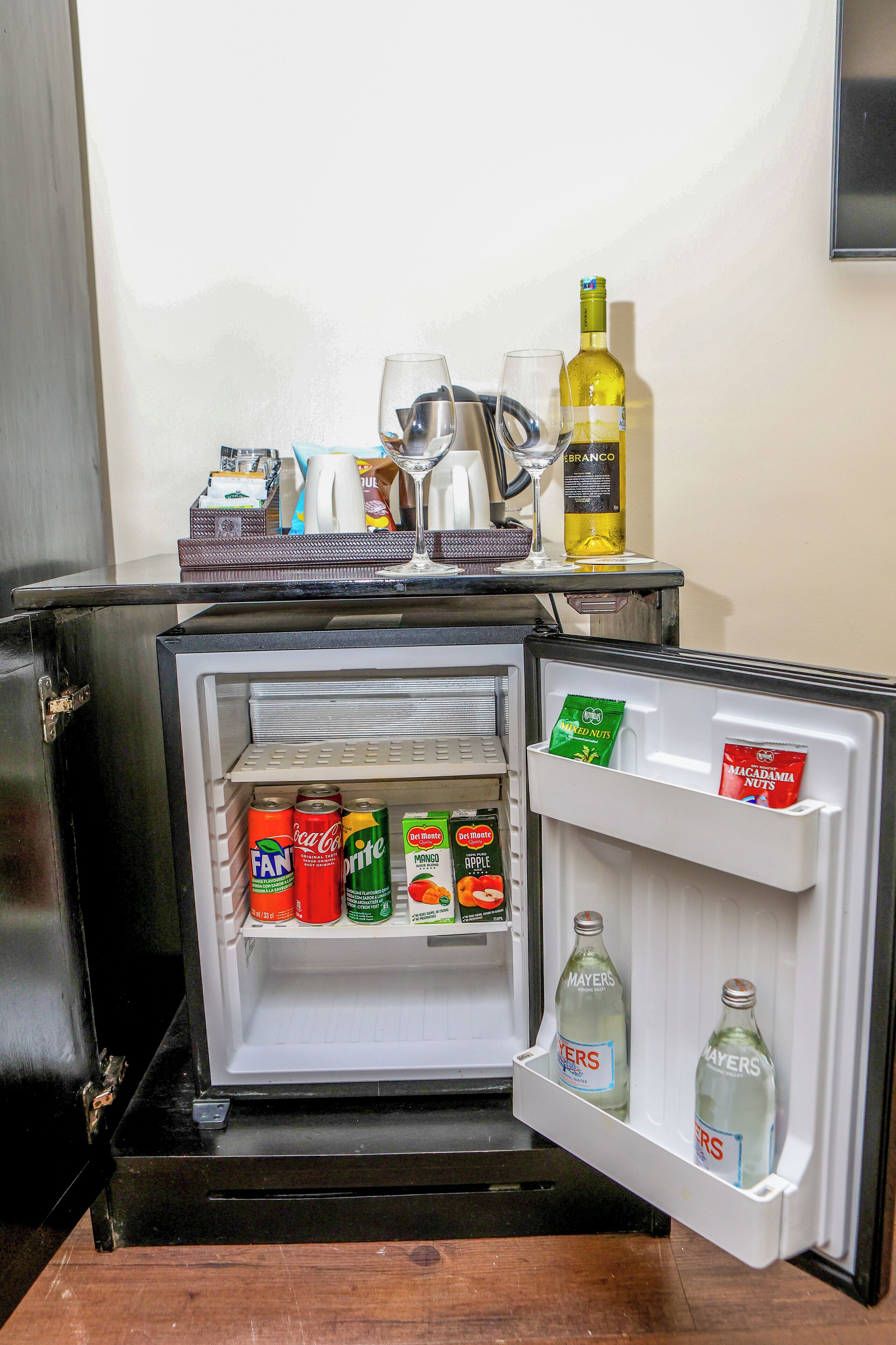 Un mini-réfrigérateur rempli de boissons et d’en-cas, une bouteille de vin et un verre à martini posés sur le dessus.