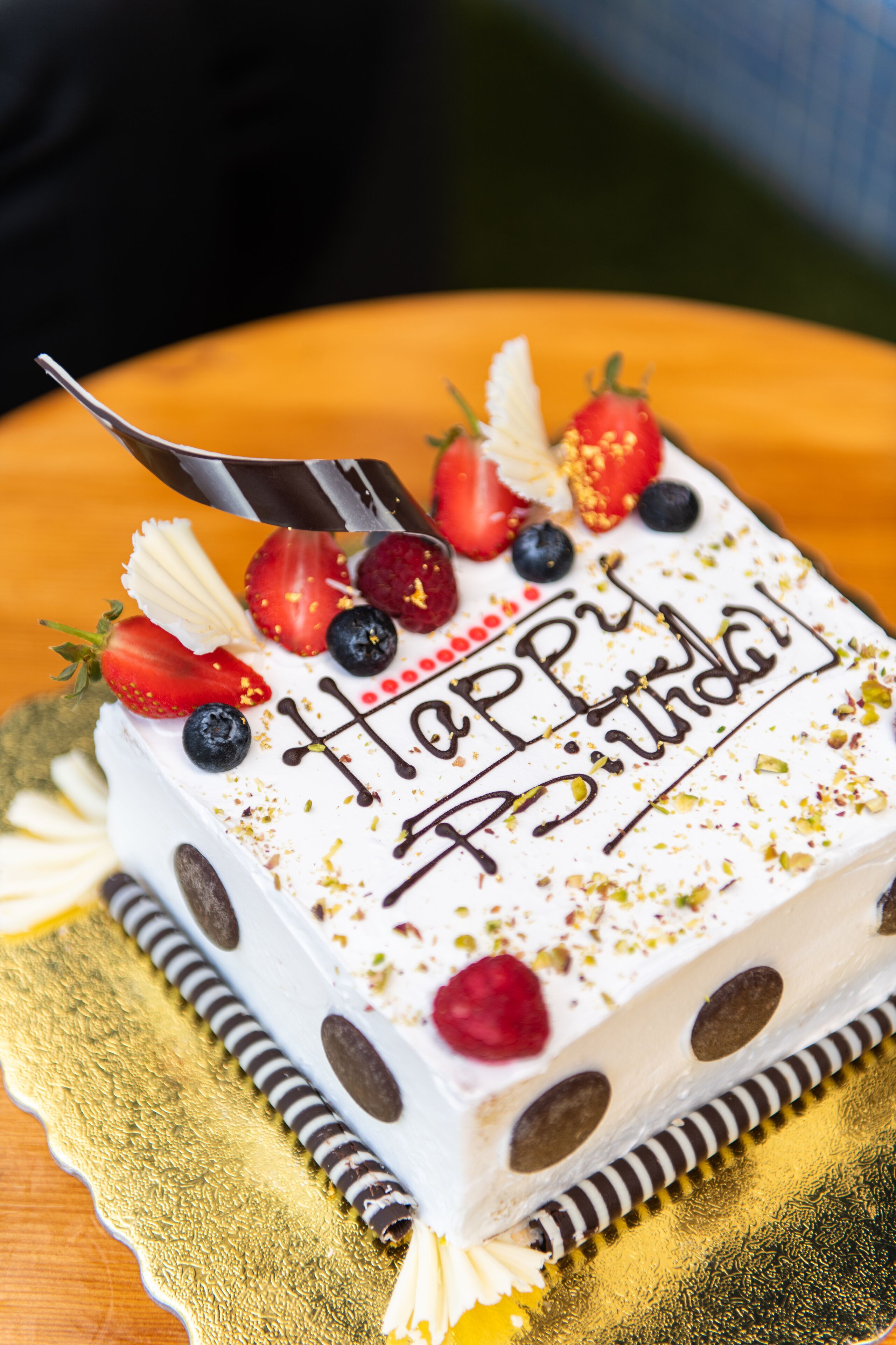 Un gâteau d’anniversaire sur lequel est écrit « Joyeux anniversaire », décoré de fraises, de myrtilles et de chocolat.