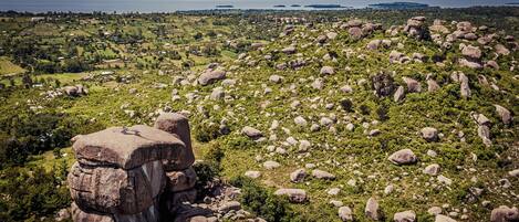 A landscape with large boulders and greenery, a clear sky, and distant water bodies.