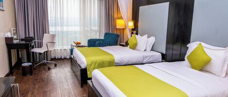 Ein Hotelzimmer mit zwei Betten, einem Schreibtisch, einem Stuhl und einem großen Fenster mit Vorhängen.