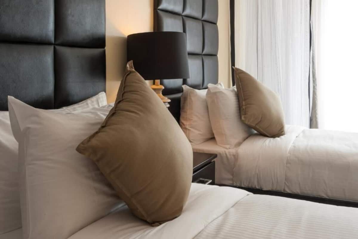 Ein Hotelzimmer mit einer gepolsterten Kopfteil, einem Nachttisch mit Lampe und mehreren Kissen.