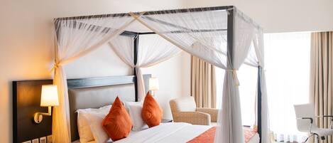 Una cama con dosel y cortinas, una mesita de noche con lámpara, una silla y un escritorio con su respectiva silla.