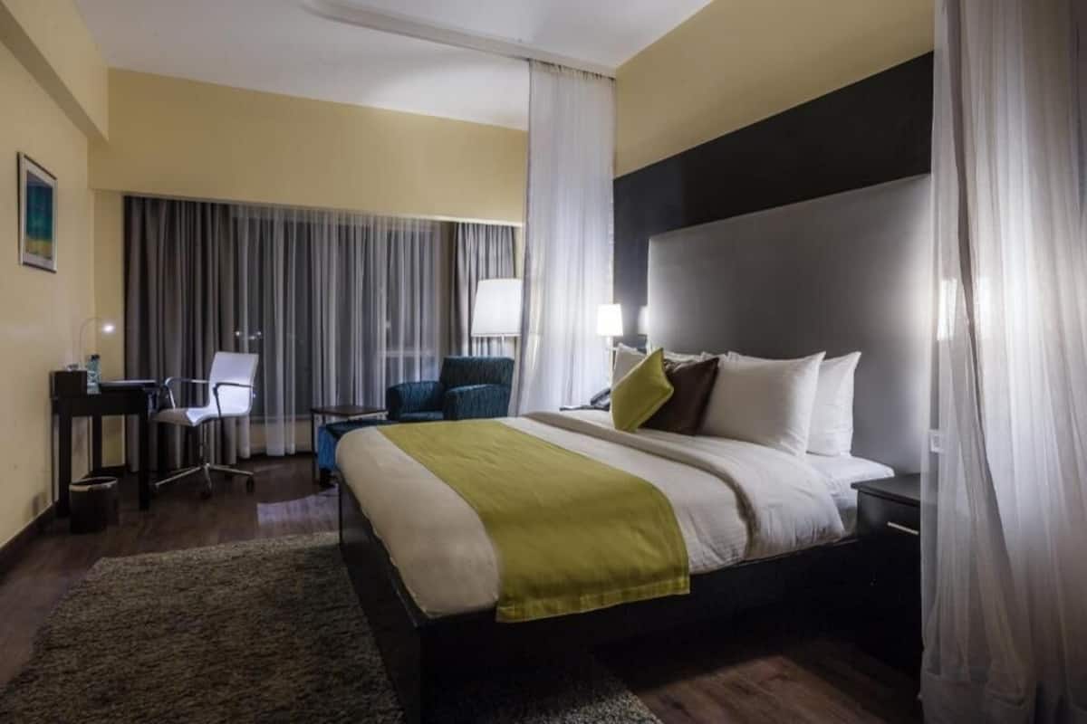 Ein Hotelzimmer mit einem Bett, einem Schreibtisch, einem Stuhl und einem großen Fenster mit Vorhängen.