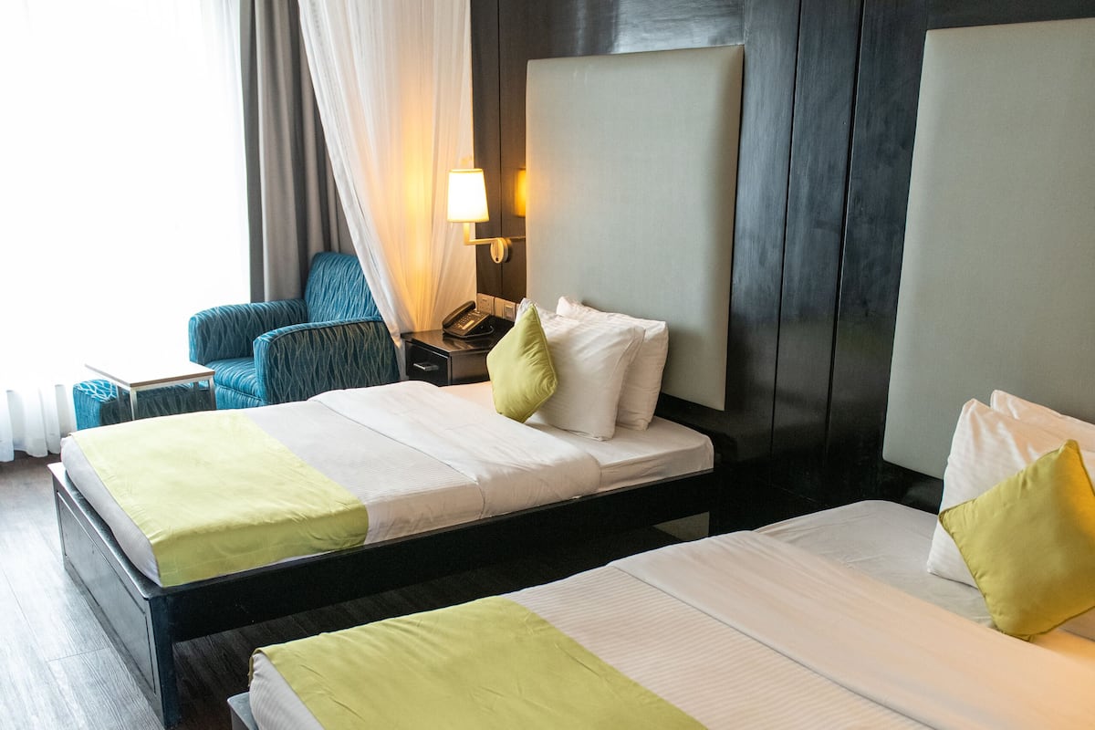 Ein Hotelzimmer mit zwei Betten, einem Nachttisch, einer Lampe und einem Sessel.