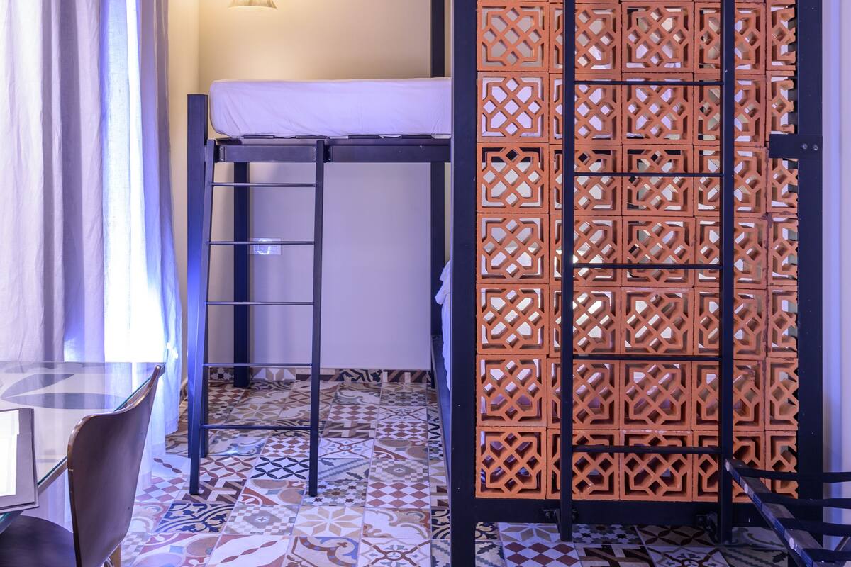 A room with a bunk bed, a table with chairs, a patterned tiled floor, and a wooden ceiling.
