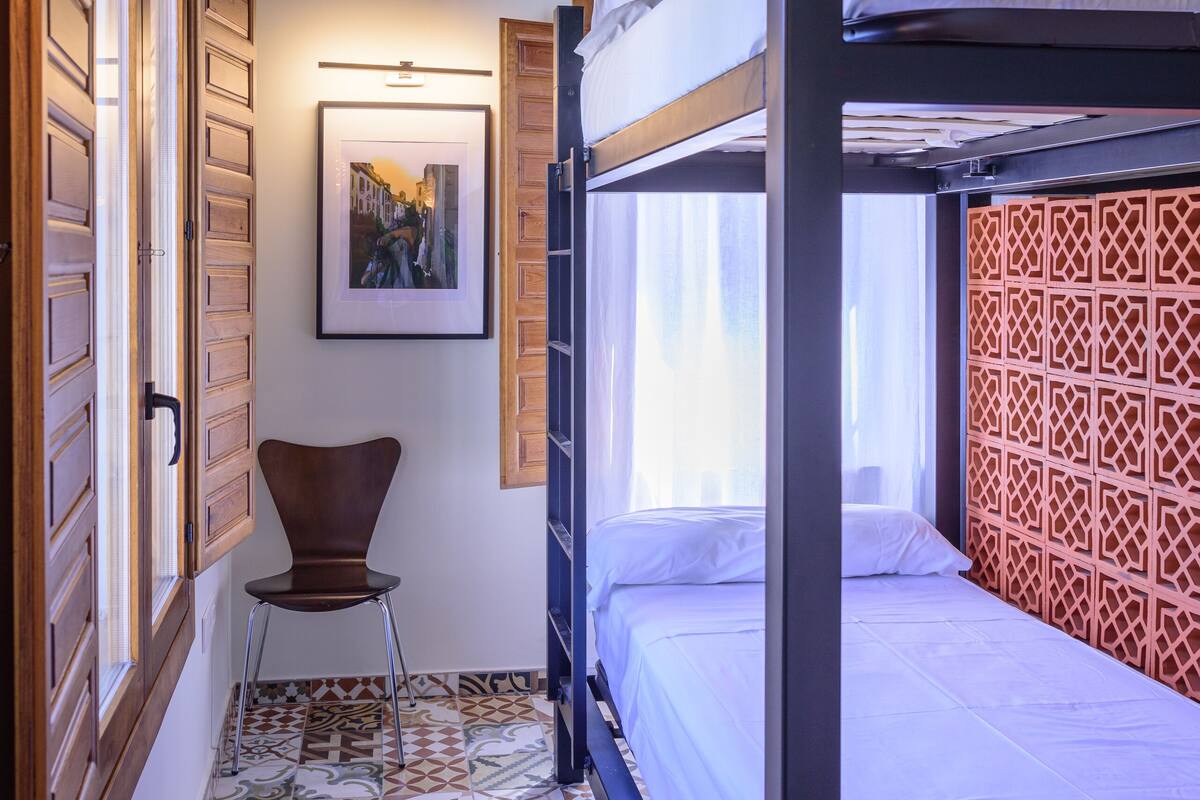 A room with a bunk bed, a chair, a patterned floor, and a framed picture on the wall.