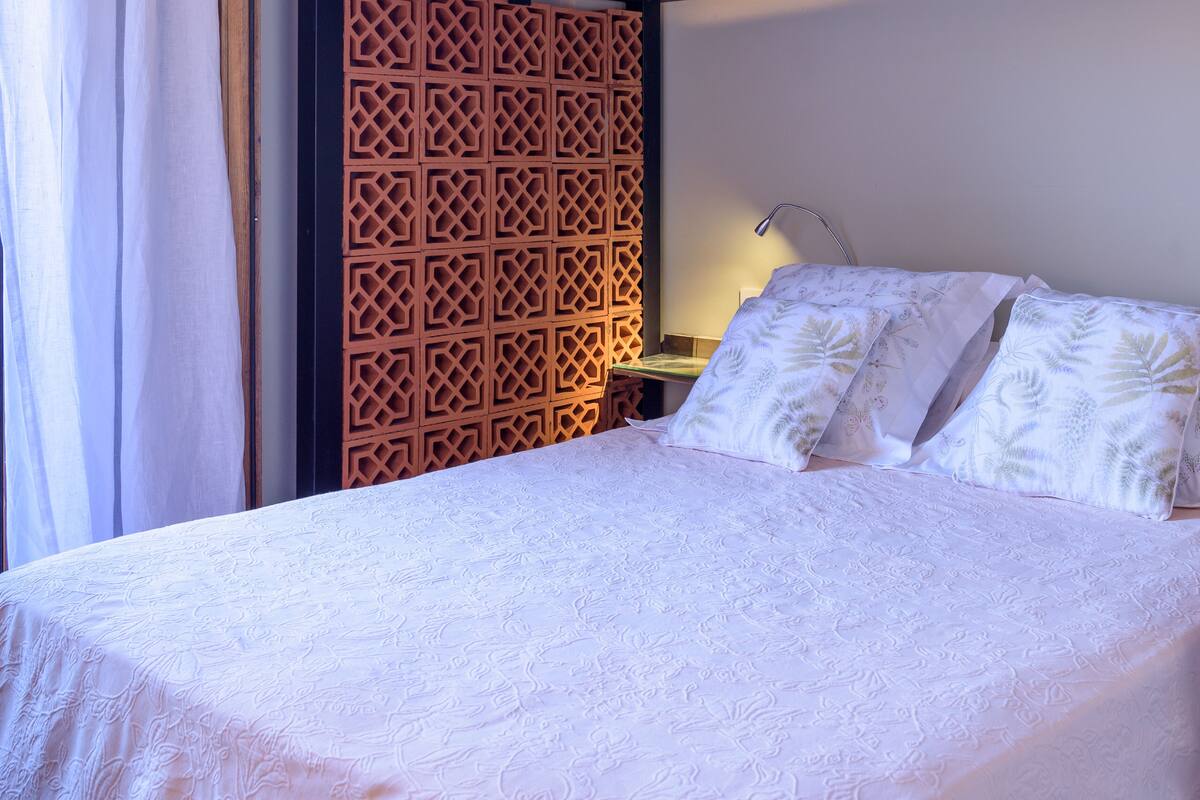 A neatly made bed with a patterned bedspread and two pillows, a wooden decorative panel, and a bedside lamp.