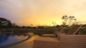 A poolside area with lounge chairs and a view of the sunset.