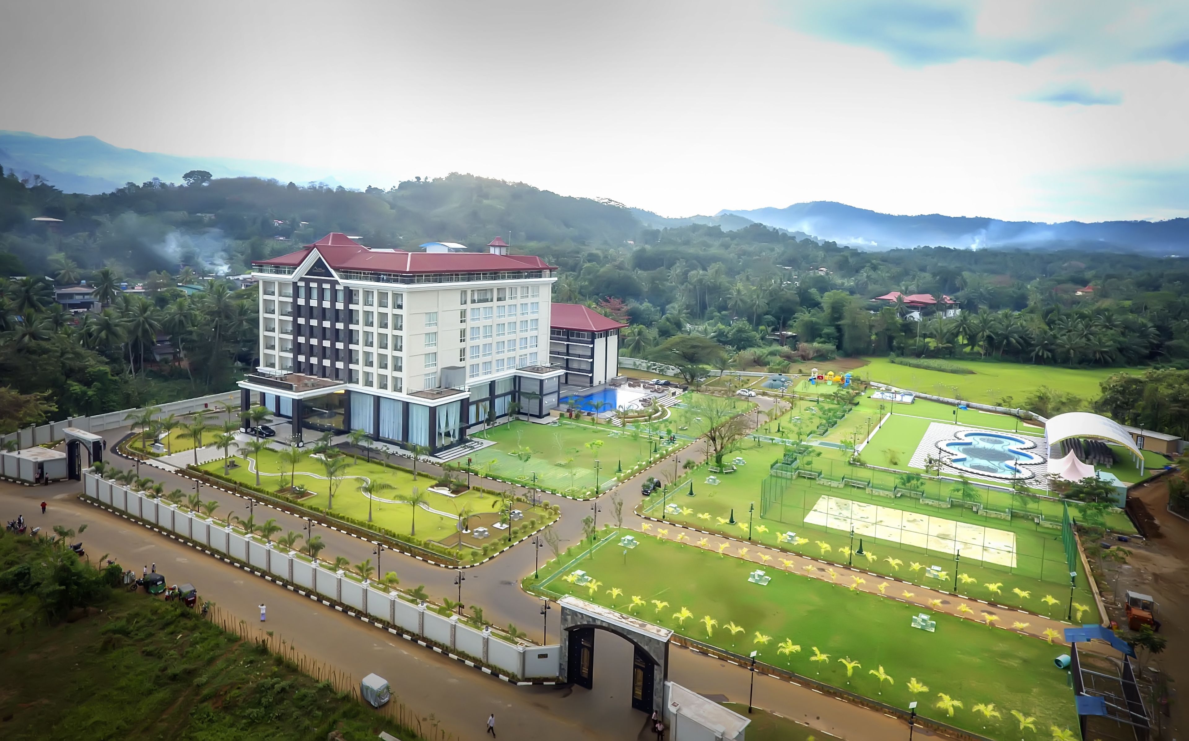 A large hotel with multiple floors, a swimming pool, and well-maintained gardens.