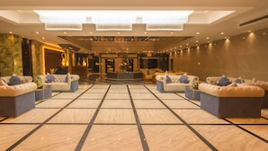 A spacious lobby with a high ceiling, marble flooring, and multiple seating areas with tufted sofas and armchairs.