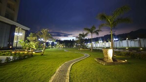 A well-lit pathway in a landscaped area with palm trees and a building in the background.