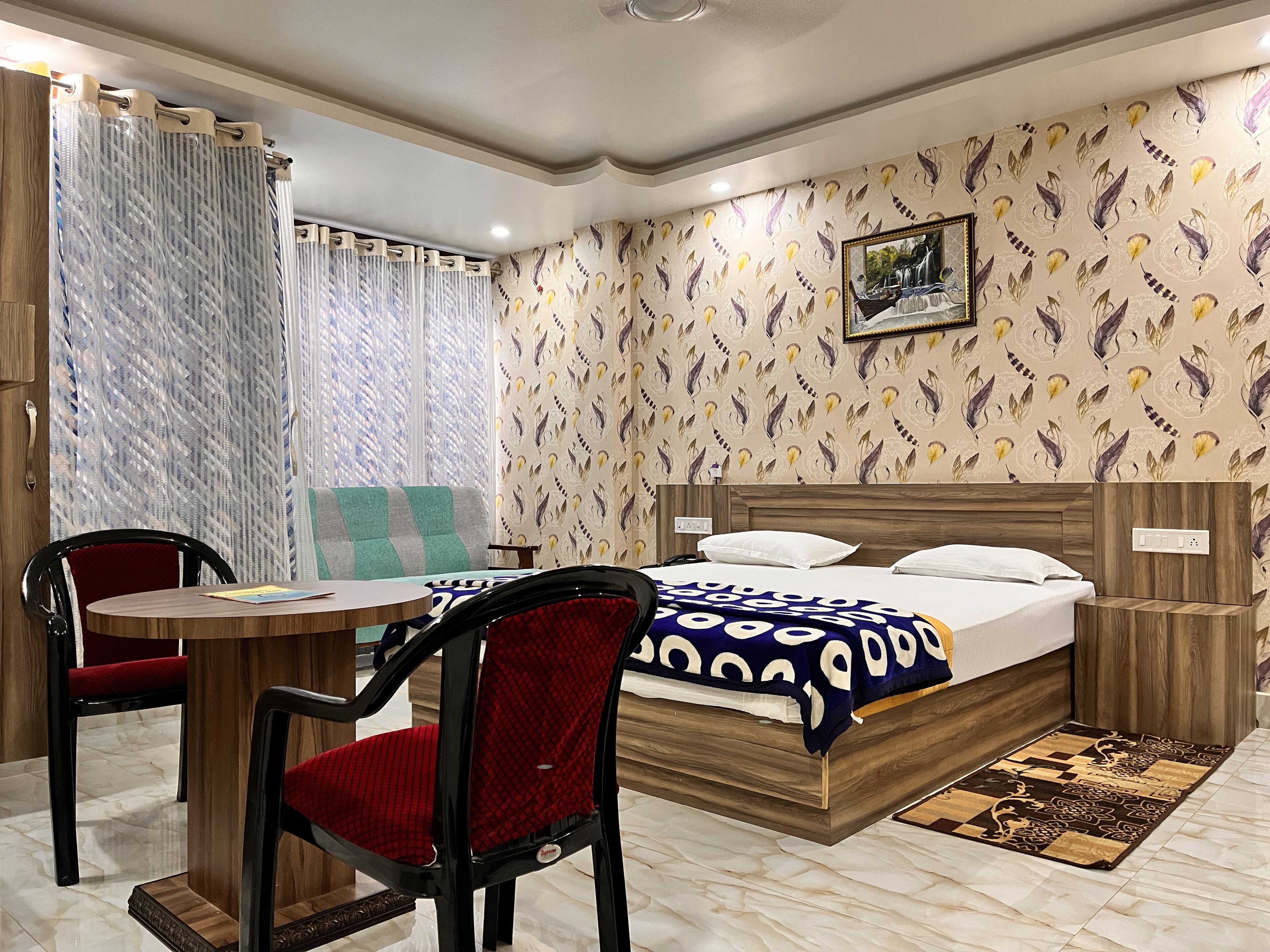 Quarto de hotel com cama, escrivaninha, duas cadeiras, janela com cortinas e papel de parede estampado.