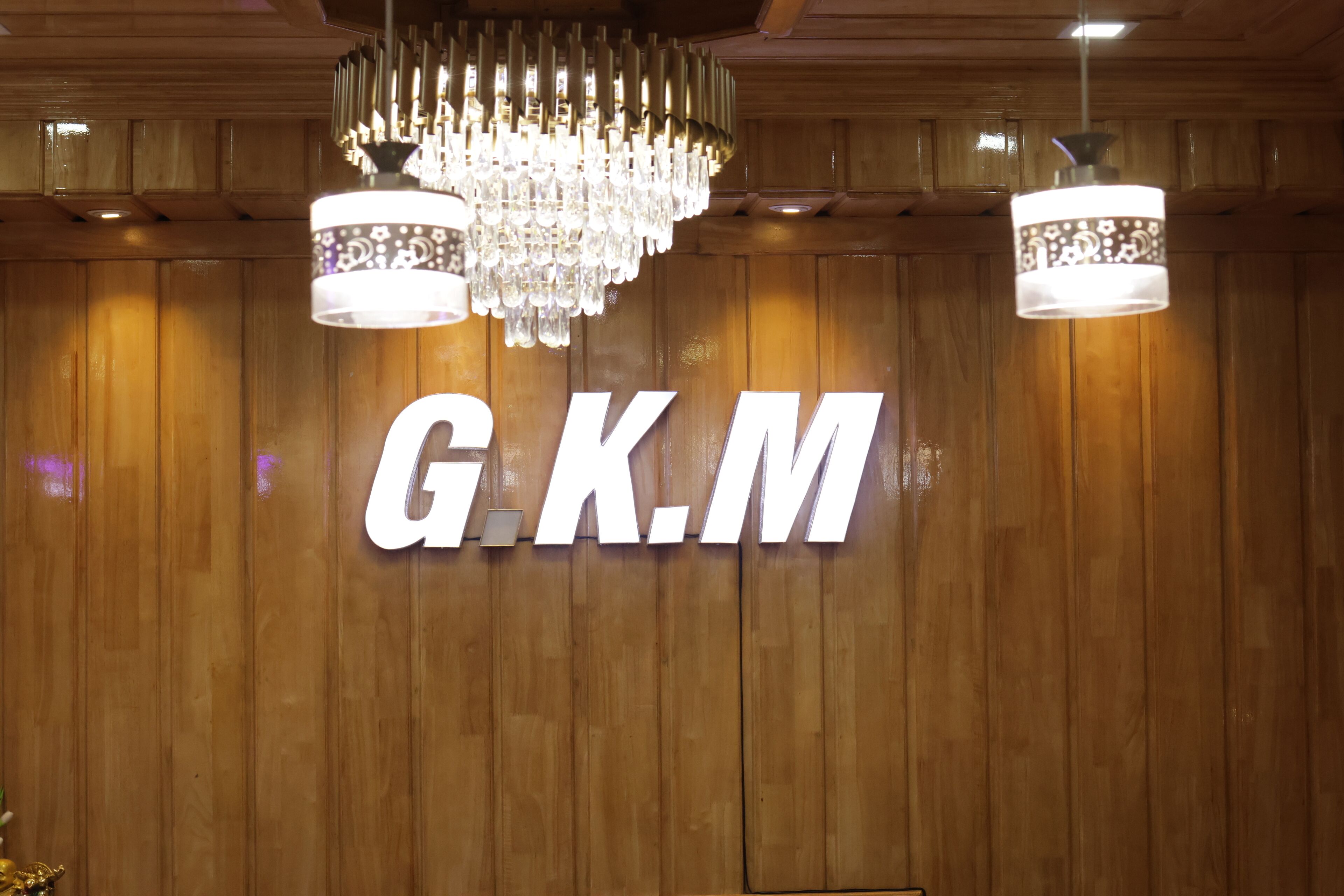 A G.K.M sign on a wooden wall with two chandeliers above it.
