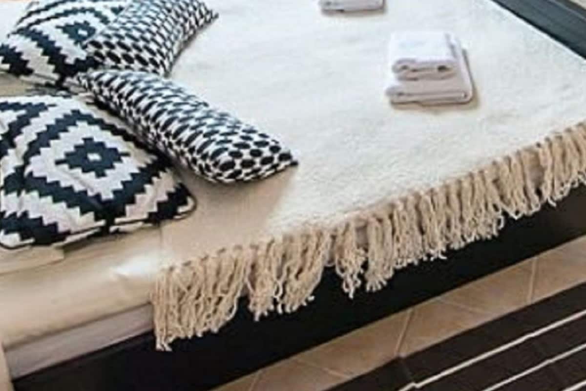 Cama com cobertura branca e franja, acompanhada por dois travesseiros estampados.