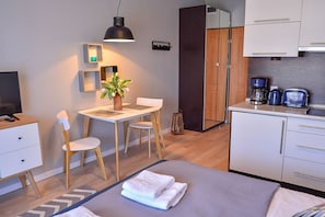 Quarto de hotel moderno com cama, escrivaninha, cadeira, mesa pequena com planta, cafeteira e guarda-roupa.