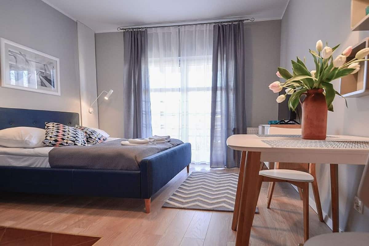 Quarto moderno com cama, escrivaninha e cadeira. Há uma janela com cortinas, um vaso com flores e um quadro na parede.