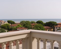 Un pueblo costero con edificios de tejados terracota, una vista despejada del mar y una barandilla de balcón en primer plano.