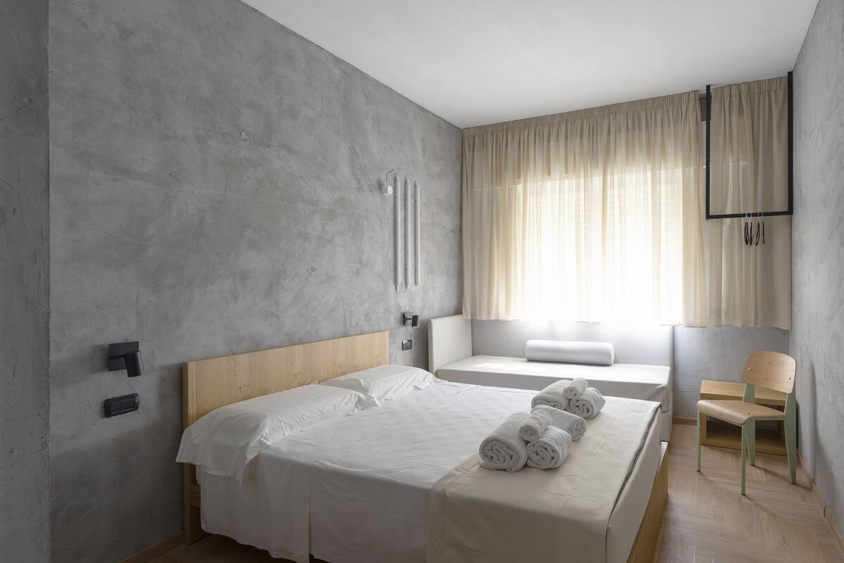 Une chambre d’hôtel moderne avec un grand lit, une table de chevet, une chaise et une fenêtre avec des rideaux.
