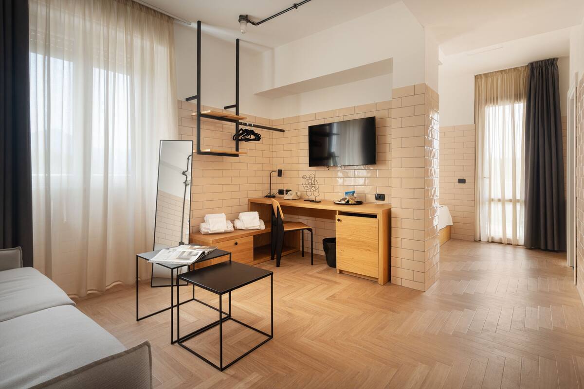 Une chambre d’hôtel moderne avec un bureau en bois, un téléviseur à écran plat, un grand miroir et un lit.