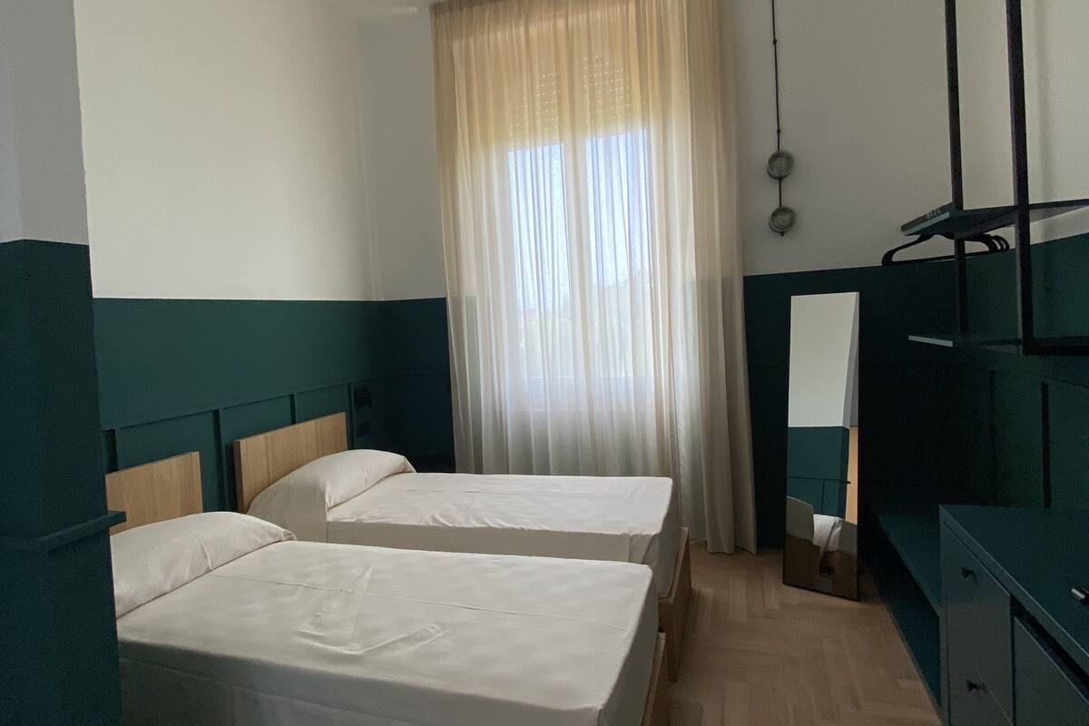 Une chambre avec deux lits simples, une tête de lit en bois, un bureau avec une chaise et un miroir au mur.