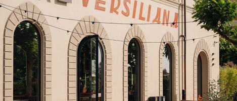 An outdoor seating area with tables and chairs in front of a building with arched windows and the name "VERSILIANI" on the facade.
