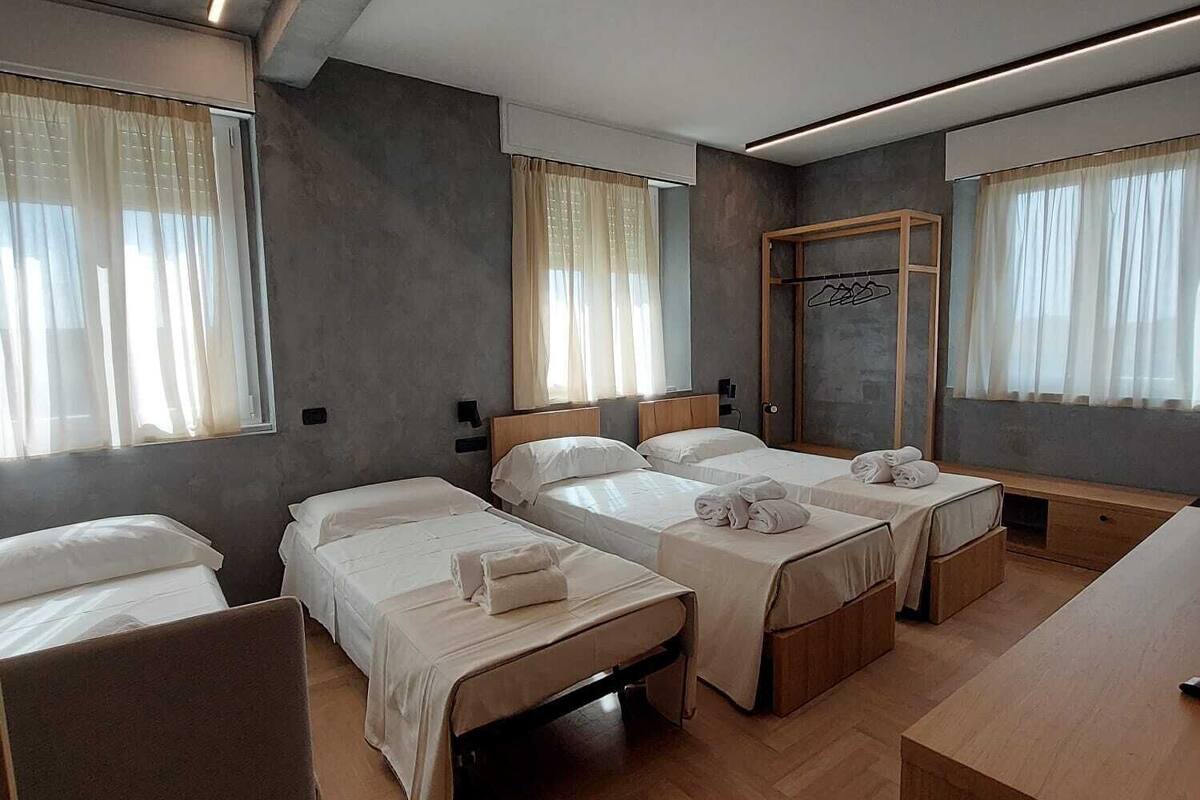 Une chambre d’hôtel avec quatre lits simples, un bureau en bois et une chaise.