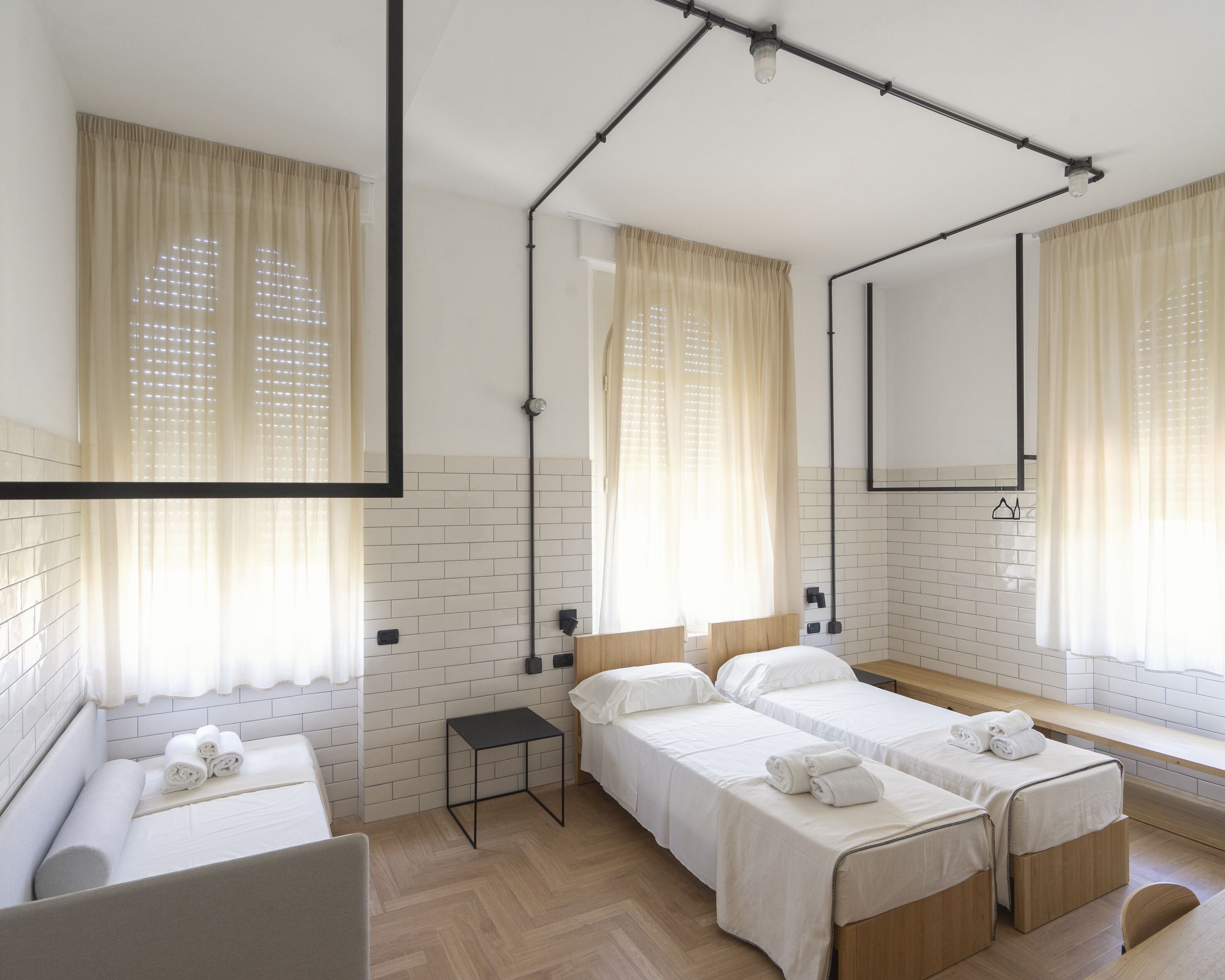 A hotel room with two beds, a small table, a mirror, and a window with curtains.
