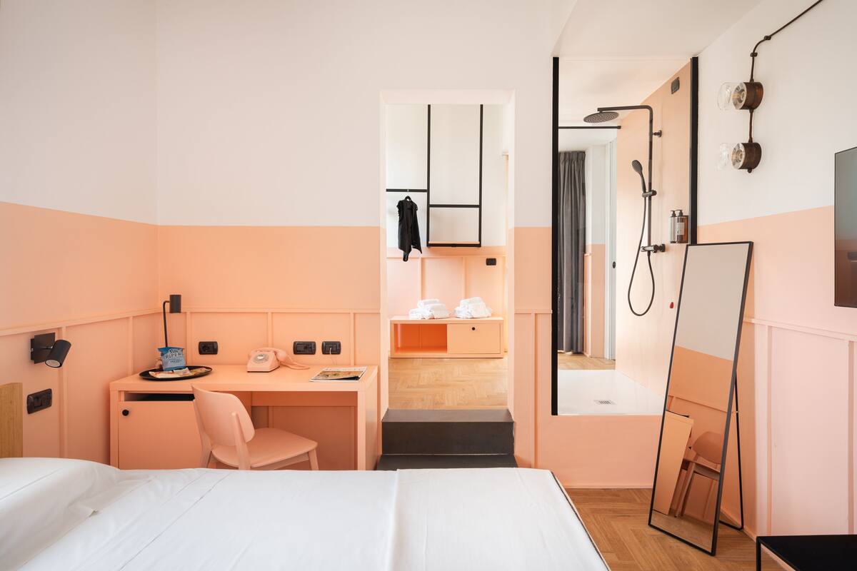 Une chambre d’hôtel comprenant un lit, un bureau, une chaise, une armoire, un miroir et un espace douche.