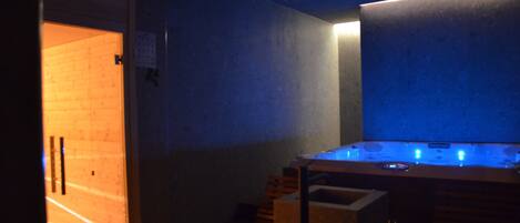 A sauna room with a wooden bench, a massage table, and a blue-lit wall.