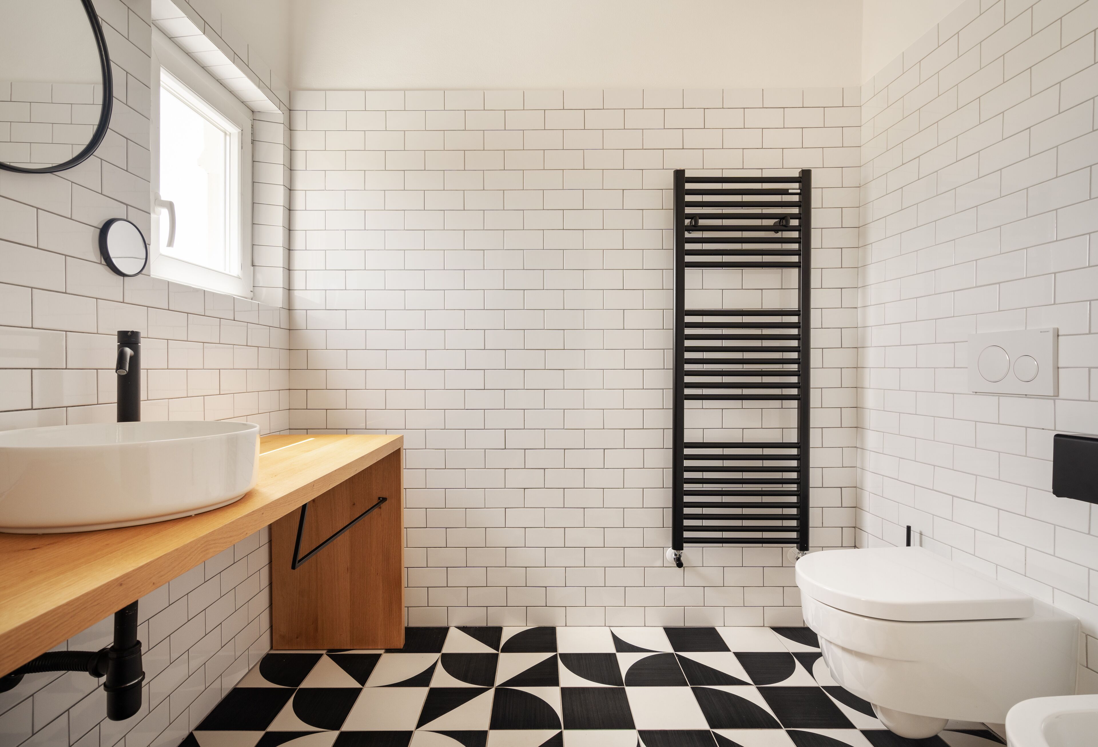A bathroom with a white sink, wooden countertop, black and white tiled floor, and a black towel rack.