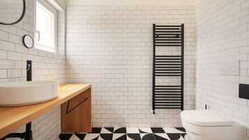 A bathroom with a white sink, wooden countertop, black and white tiled floor, and a black towel rack.