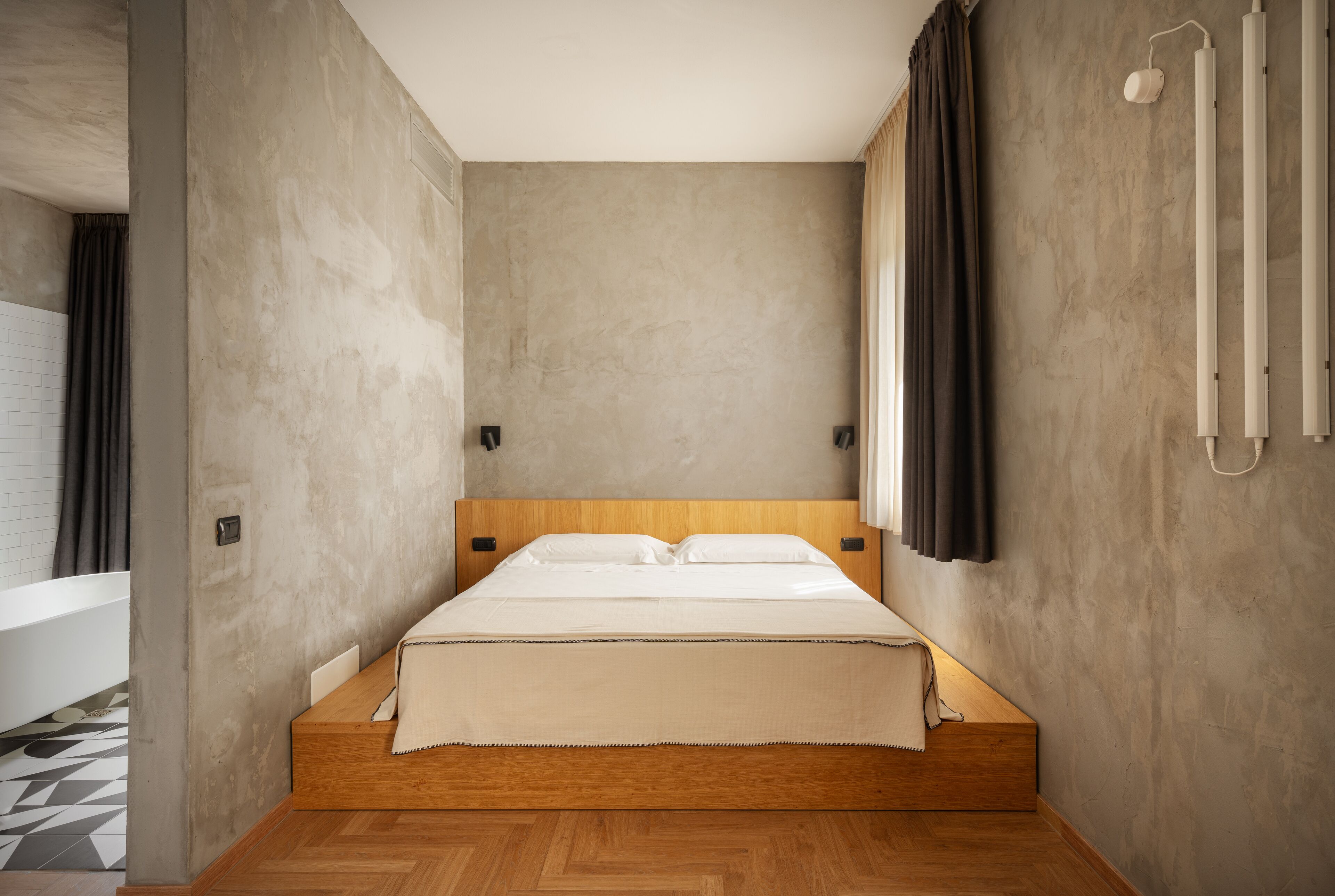 A modern bedroom with a wooden bed, a large window with curtains, and a visible bathroom with a bathtub.