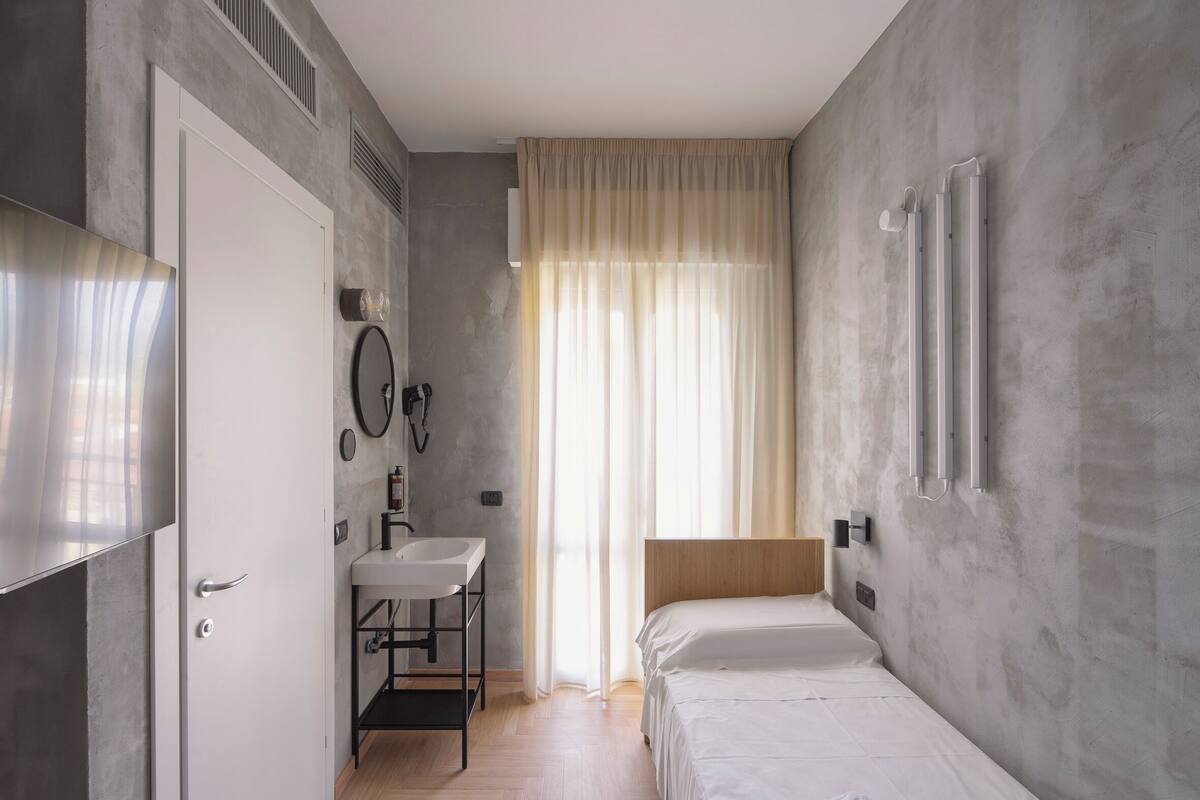 Une chambre à coucher avec un lit, une table de chevet, un miroir et une fenêtre avec des rideaux.